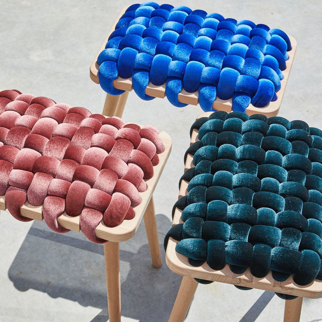 Velvet woven stools in sapphire blue, rose, and emerald, featuring natural wood legs