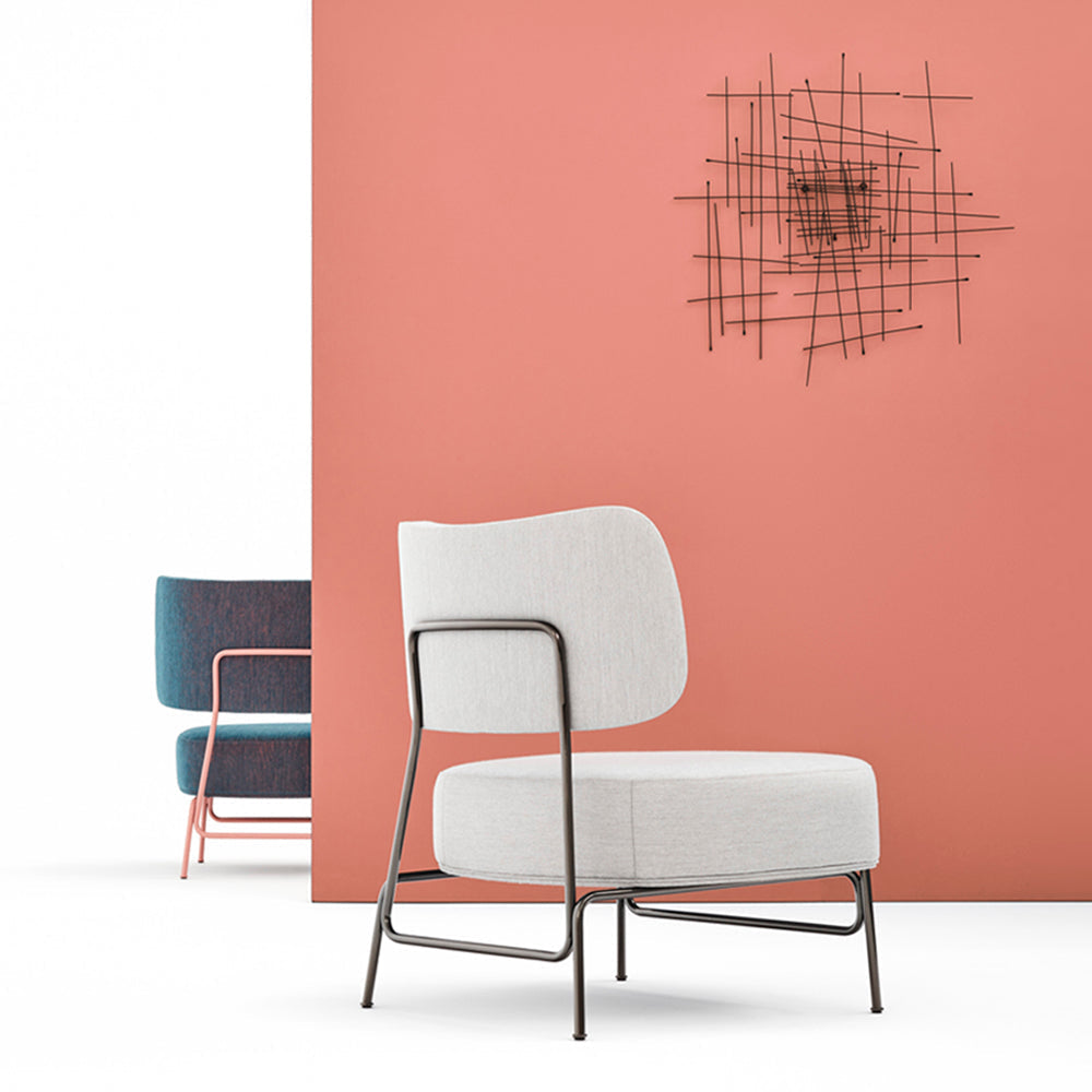 Modern lounge chair with light grey upholstery and sleek metal frame, set against a coral wall