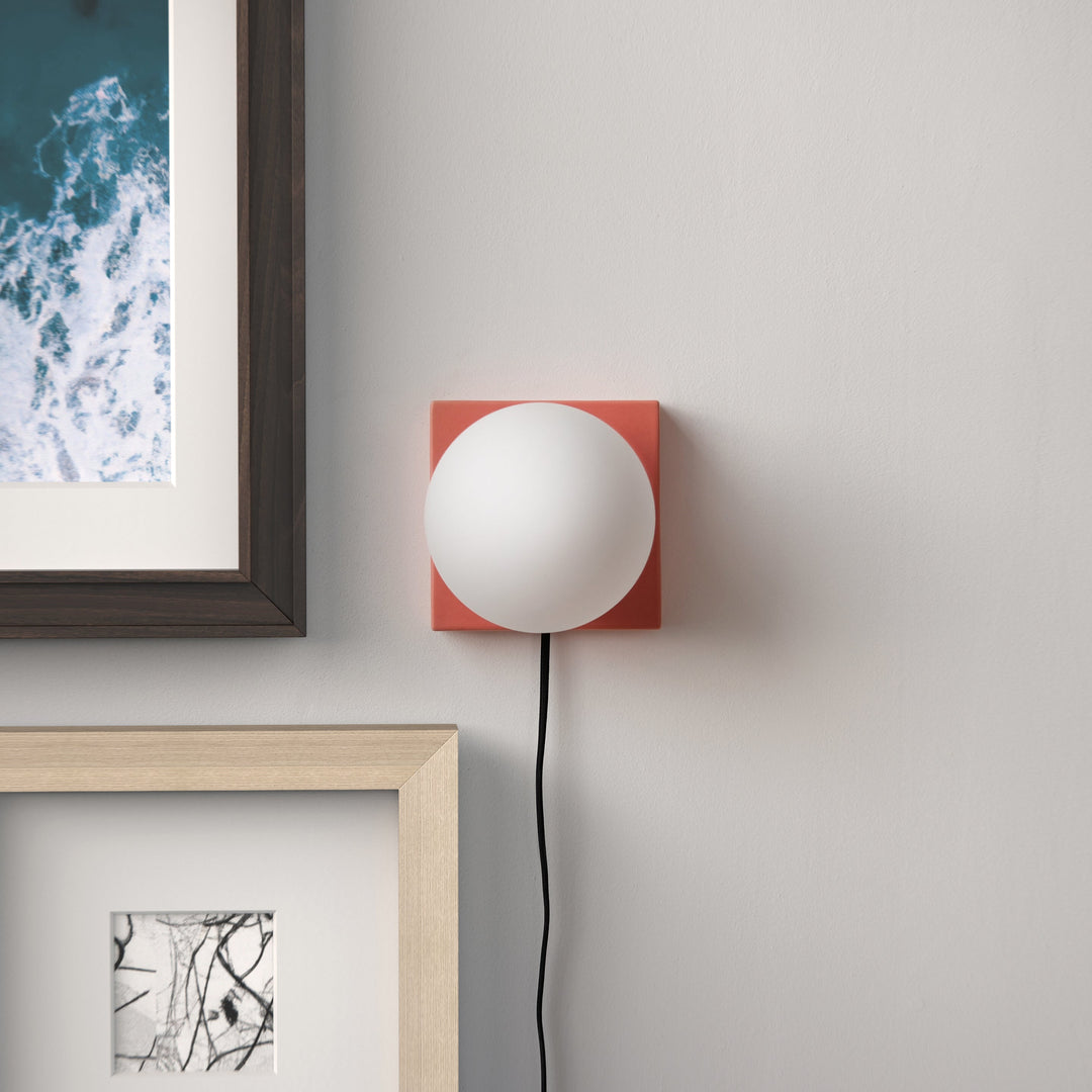 Coral wall sconce with frosted glass globe, minimalist modern design above framed art