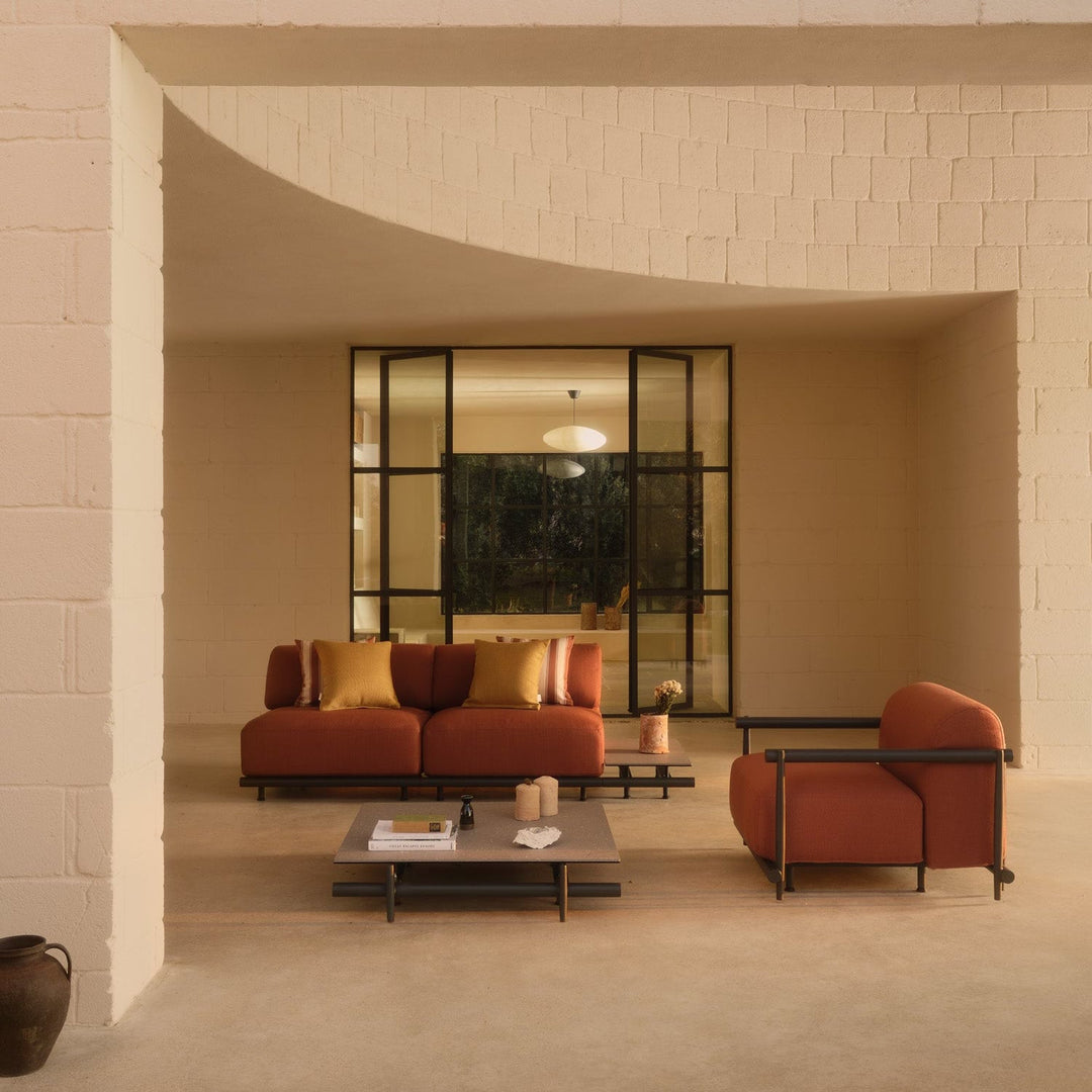 Rust-hued modular sofa and armchair with metal frames in a modern sunlit lounge setting