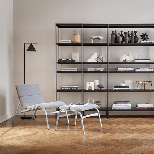 Modern accent lounge chair with ottoman in soft gray fabric, minimalist shelving, sculptural decor