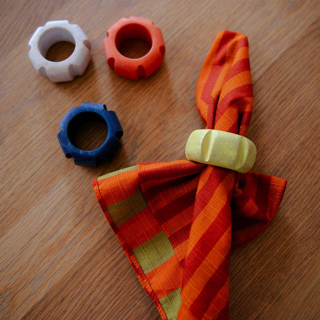 Handpainted wood napkin rings in assorted colors on a striped linen napkin, atop a wooden table.
