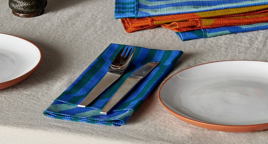 Stoneware plates with terracotta rim, stainless cutlery on striped woven napkin, linen tablecloth