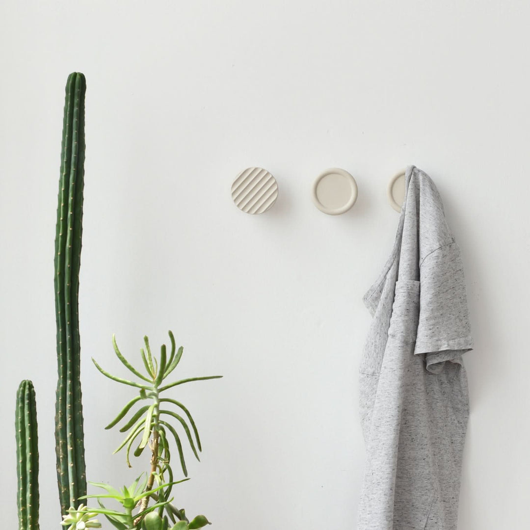 Minimalist ceramic wall hooks with ribbed detail beside green cactus and grey shirt