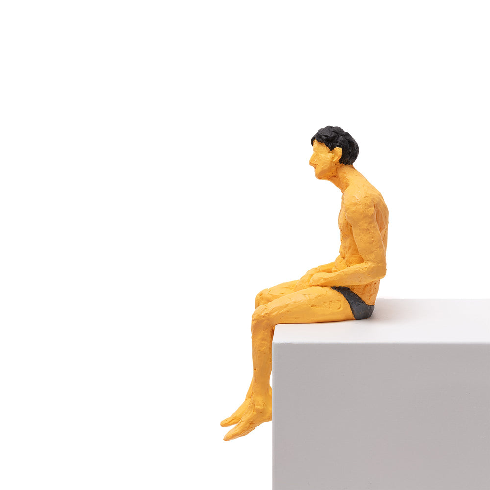Seletti Love Is a Verb Alberto Figurine, side view of the seated figure leaning forward over the edge