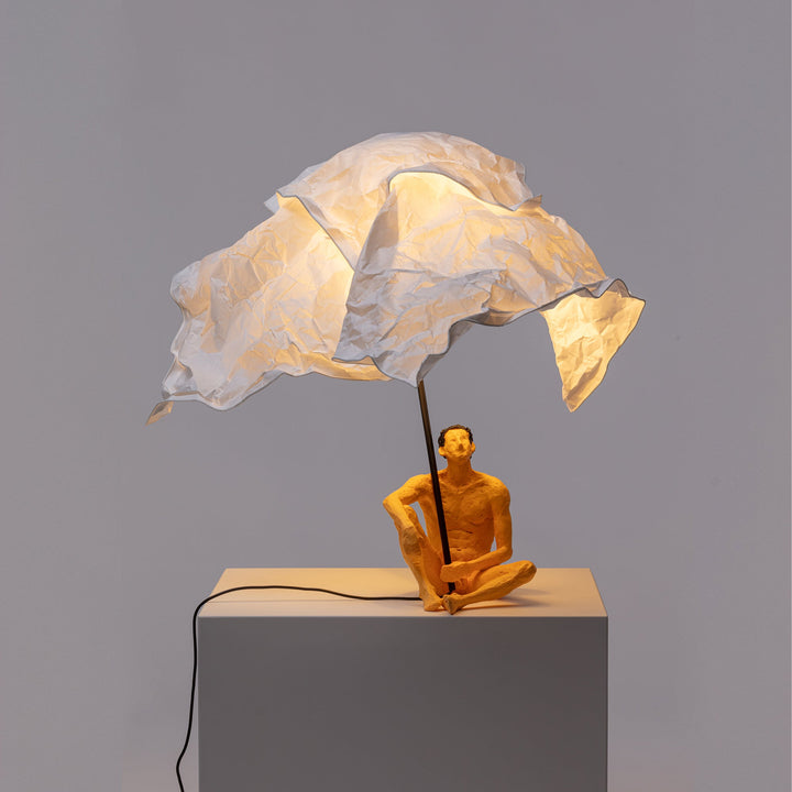 Seletti Love Is a Verb Lamp Roby, glowing shade over the seated man on a gray plinth