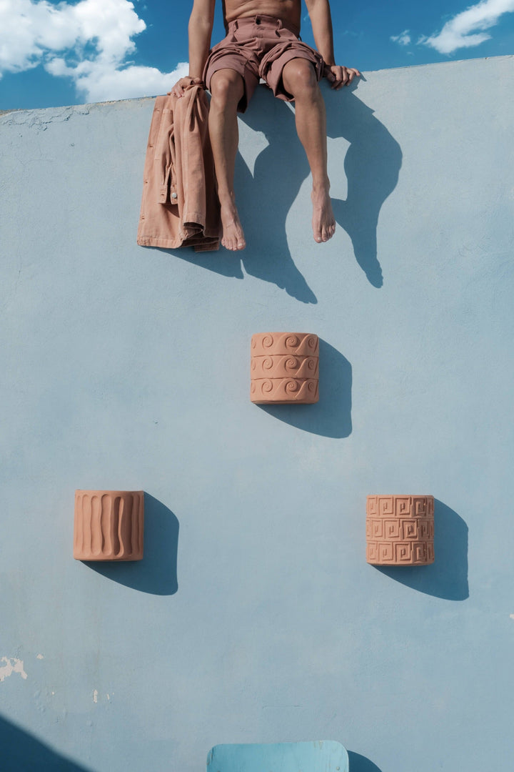 Seletti Magna Graecia Terracotta Wall Vase Onde, three wall vases on a blue wall below a seated figure