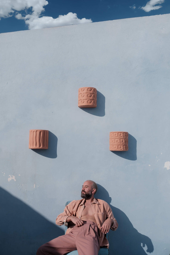 Seletti Magna Graecia Terracotta Wall Vase Greche, three wall vases hung above a man seated on a terrace