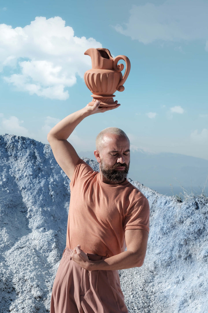 Seletti Magna Graecia Terracotta Caraffa, a man holding the jug overhead on a rocky coast