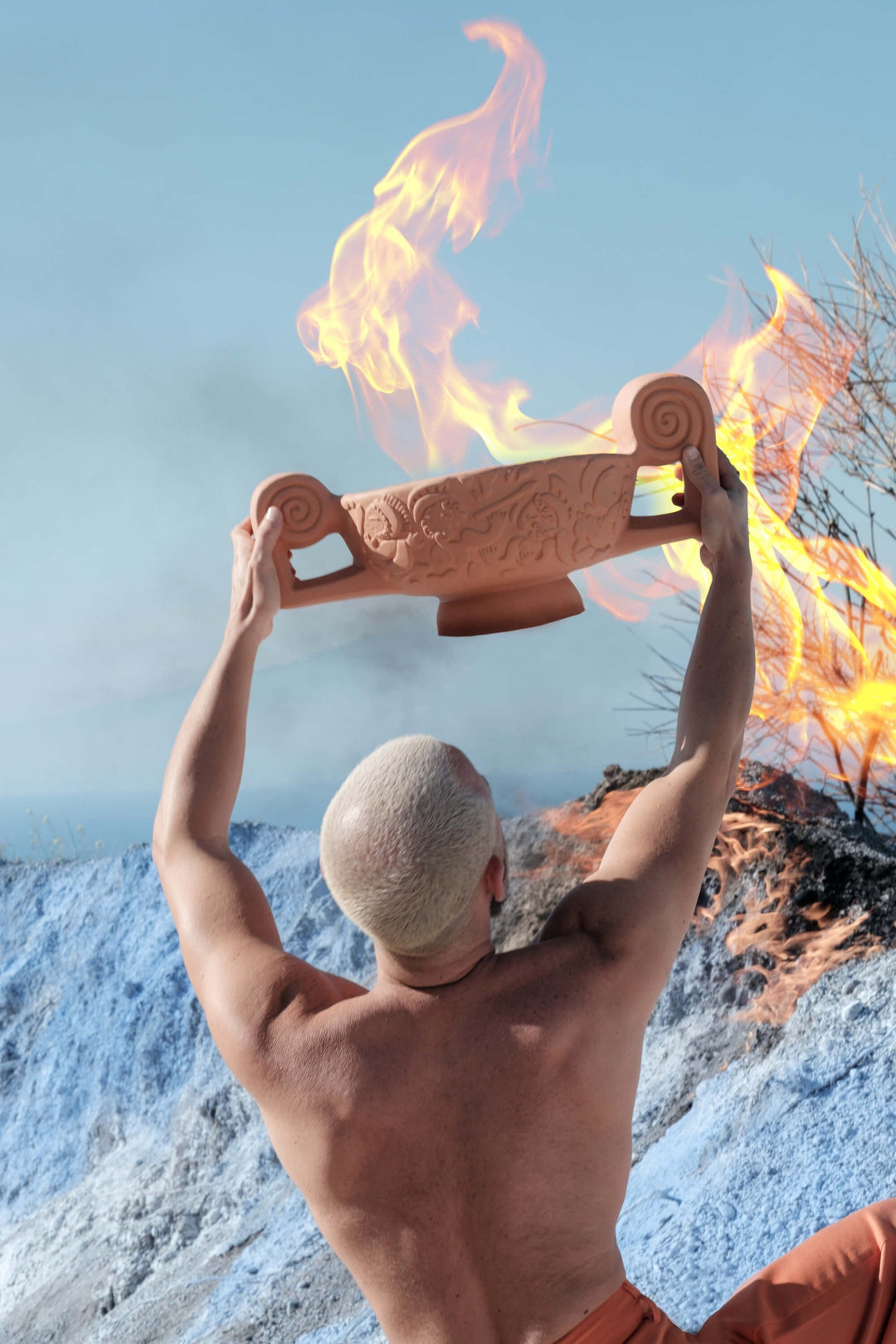 Seletti Magna Graecia Terracotta Centerpiece, a man raising the centerpiece overhead against flames and sky