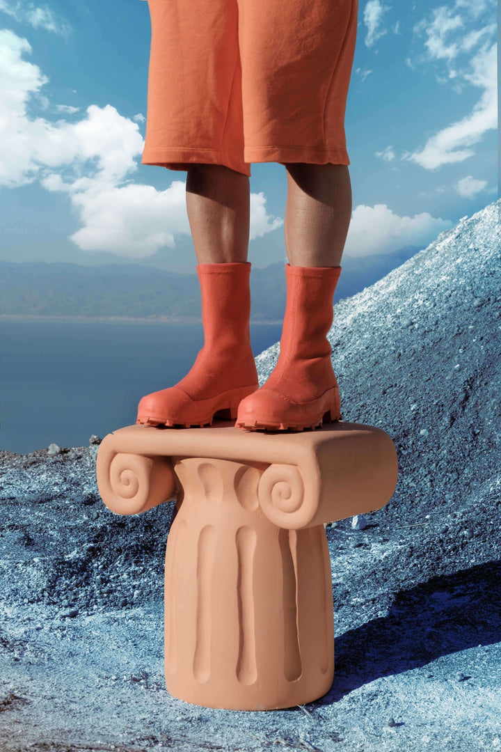 Seletti Magna Graecia Terracotta Capitello Stool, a person in orange socks standing on the capital against a coastal sky
