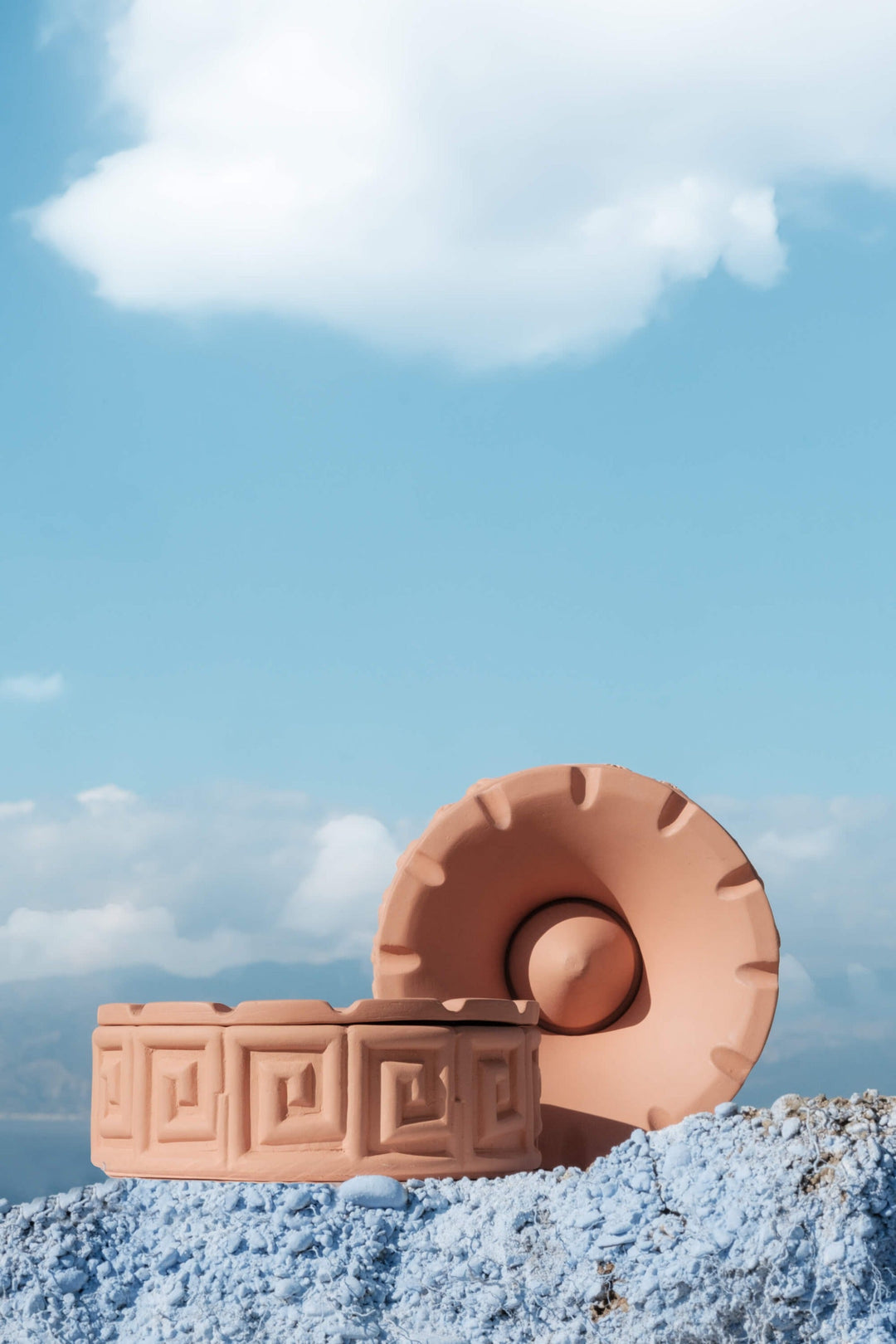 Seletti Magna Graecia Terracotta Ashtray Greche, the ashtray and its lid styled on a blue rock under a summer sky