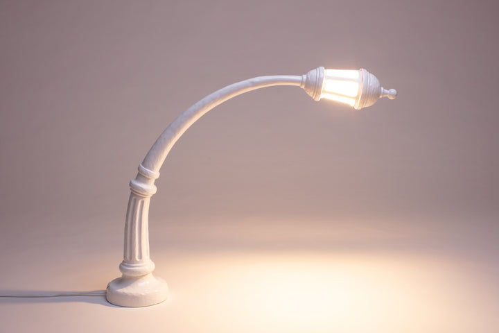 Seletti Sidonia Desk Lamp White, the white lamp lit, its lantern casting warm light on a mauve backdrop