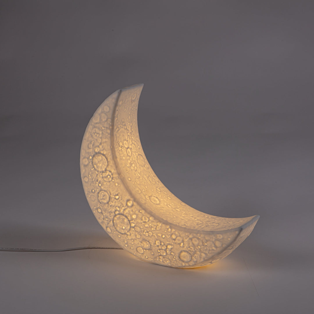 Seletti My Tiny Moon Lamp, the lit crescent on a dark gray backdrop, craters showing through