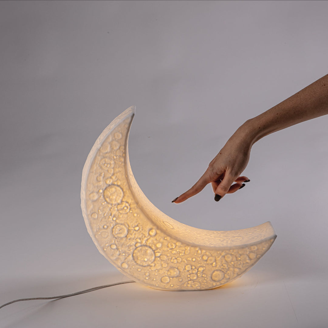 Seletti My Tiny Moon Lamp, a finger touching the glowing crescent moon lamp
