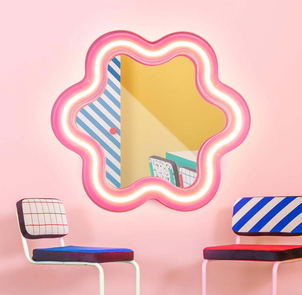 Seletti Supercurve Wavy Mirror Flower, the lit flower mirror on a pink wall above two chairs