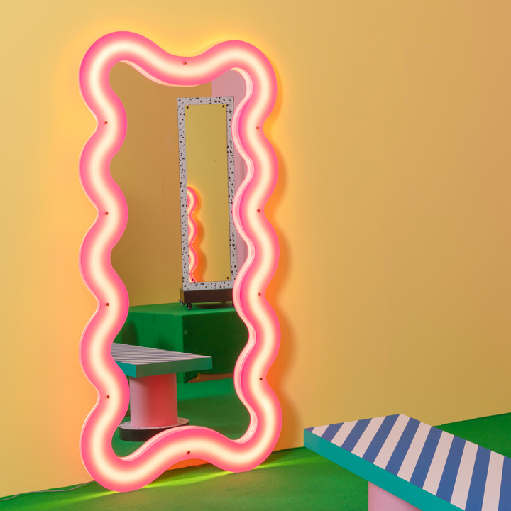 Seletti Supercurve Wavy Mirror Tall, the tall mirror glowing pink, leaning against a yellow wall