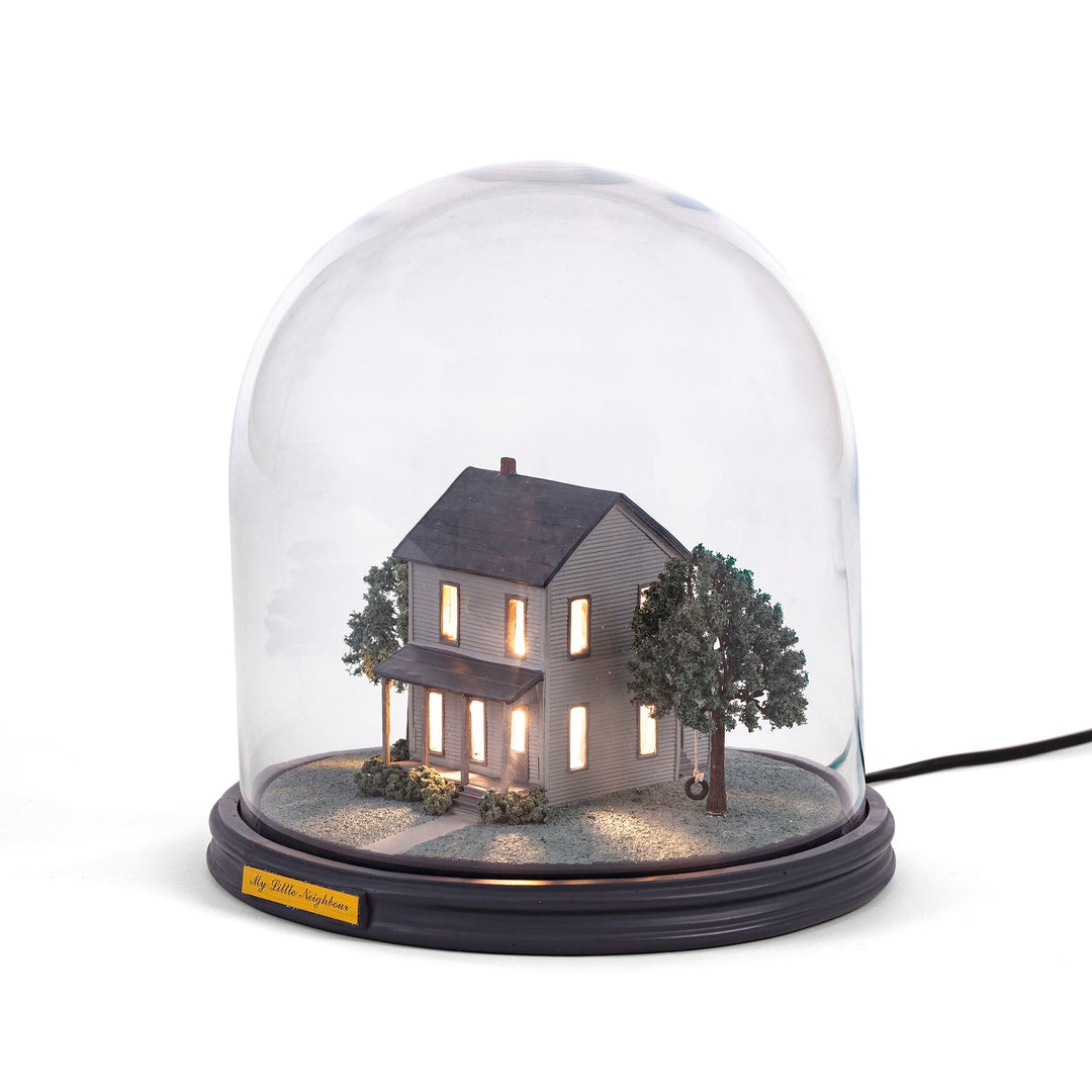 Seletti My Little Neighbour, two-story clapboard house with lit windows and trees under a glass dome
