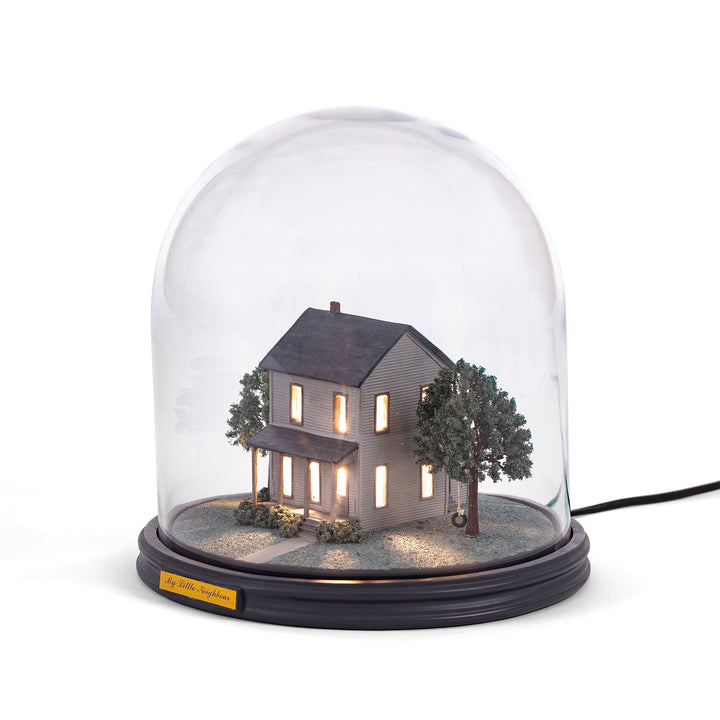 Seletti My Little Neighbour, two-story clapboard house with lit windows and trees under a glass dome