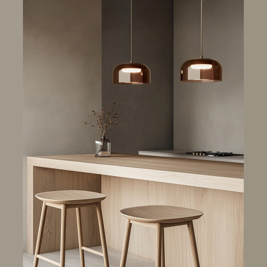 Two Ipon pendants in amber glass lit above a pale wood kitchen counter with stools
