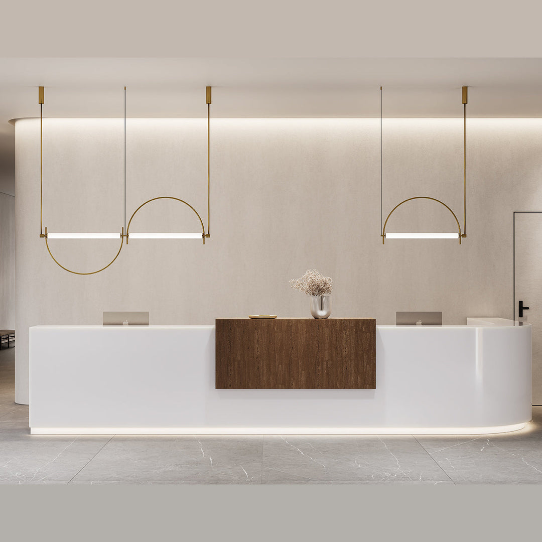 Three Arc Pendant Lamps in aged gold, lit, hung in a row above a curved white reception desk