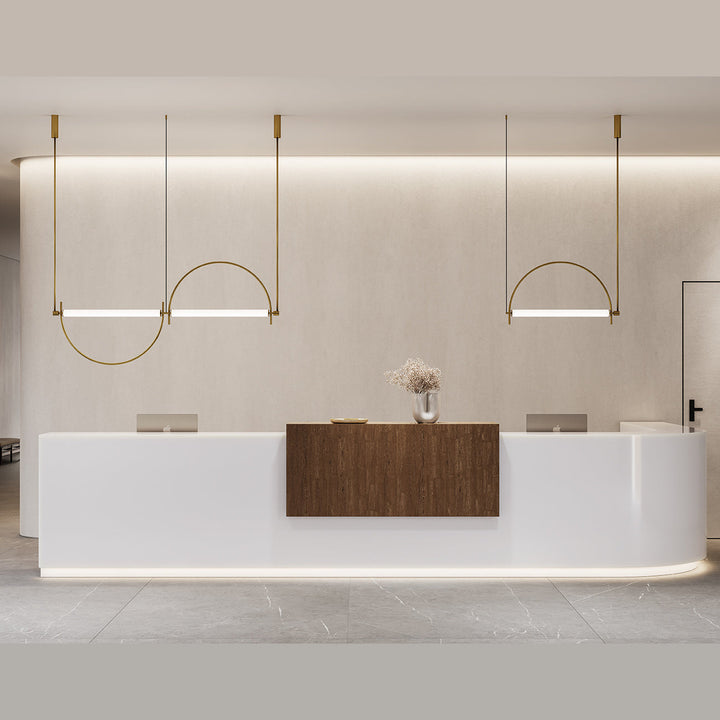 Three Arc Pendant Lamps in aged gold, lit, hung in a row above a curved white reception desk