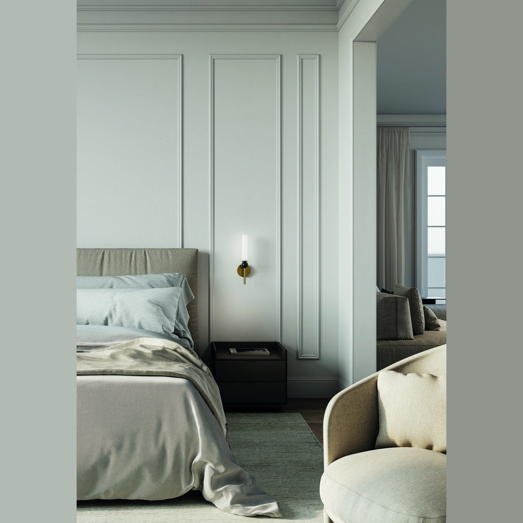 Aged gold Delie Wall Lamp lit beside a bed in a pale green panelled bedroom