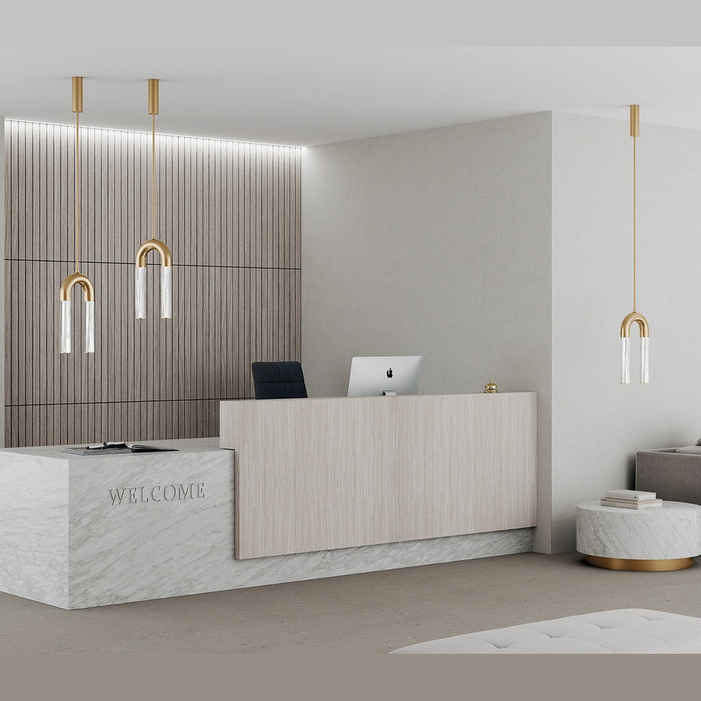 Iman Pendant Lamp in aged gold, three hung over a marble reception desk in a pale lobby