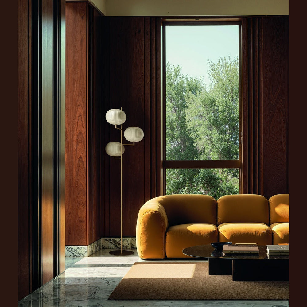 Irzo Floor Lamp in aged gold beside a curved mustard sofa and tall window in a wood-panelled room