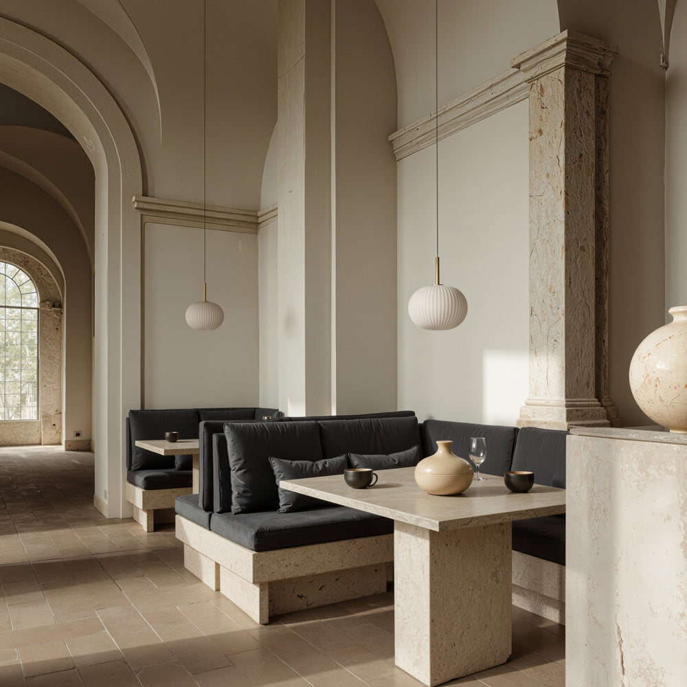Two Irzo pendants lit above stone dining tables and dark banquettes in an arched hall