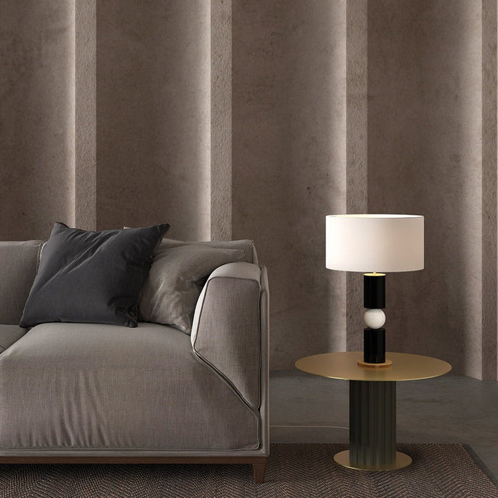 Alda Table Lamp lit on a brass side table beside a grey sofa