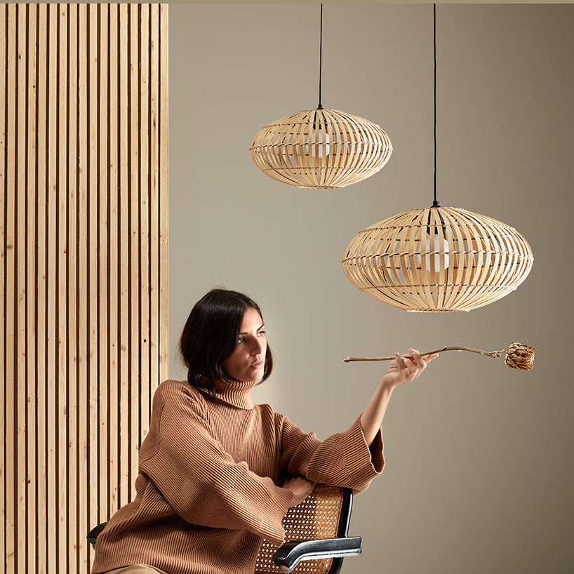 Anya Pendant Lamp pair hung at staggered heights above a woman in a cane chair by a wood slat wall