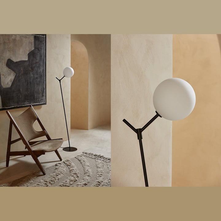 Atom Floor Lamp in black beside a wooden lounge chair and abstract painting, plus a close-up of the opal globe