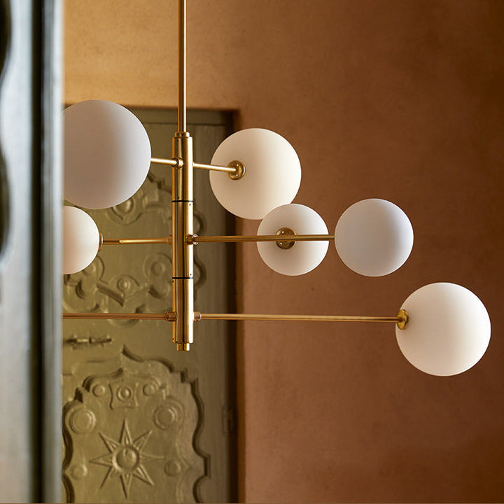 Atom Chandelier in brass with opal globes hanging in a terracotta-walled hallway beside an ornate carved door