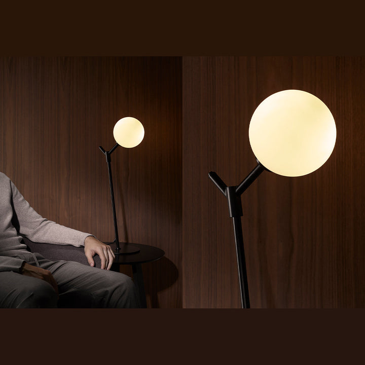 Atom Table Lamp in black, lit, on a side table beside a seated man against walnut panelling, plus a globe close-up
