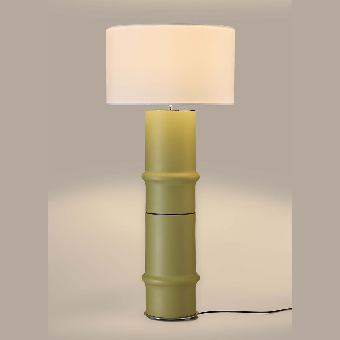 Bambu Floor Lamp in soft olive green, lit, casting a warm glow on a taupe backdrop