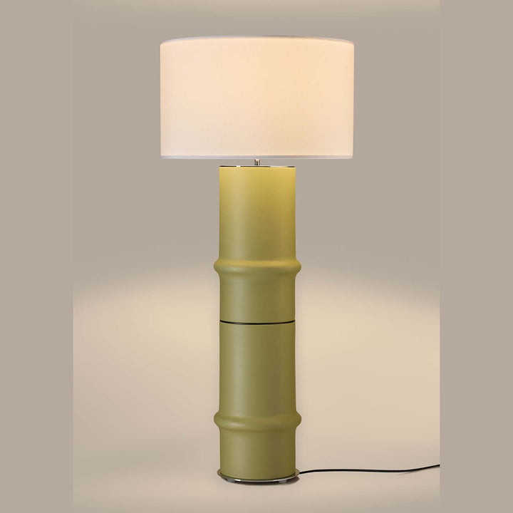 Bambu Floor Lamp in soft olive green, lit, casting a warm glow on a taupe backdrop