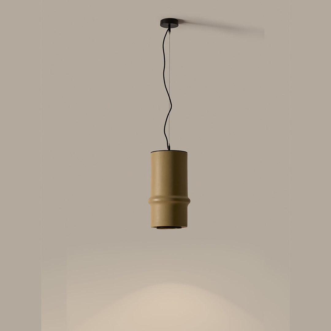 Bambu Pendant in olive-sand ceramic, lit, casting a pool of light below against a taupe wall