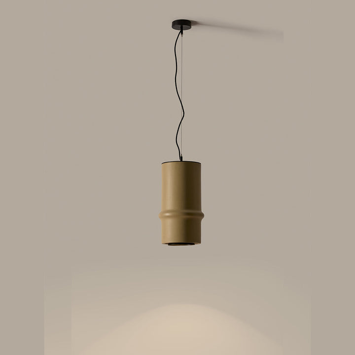 Bambu Pendant in olive-sand ceramic, lit, casting a pool of light below against a taupe wall