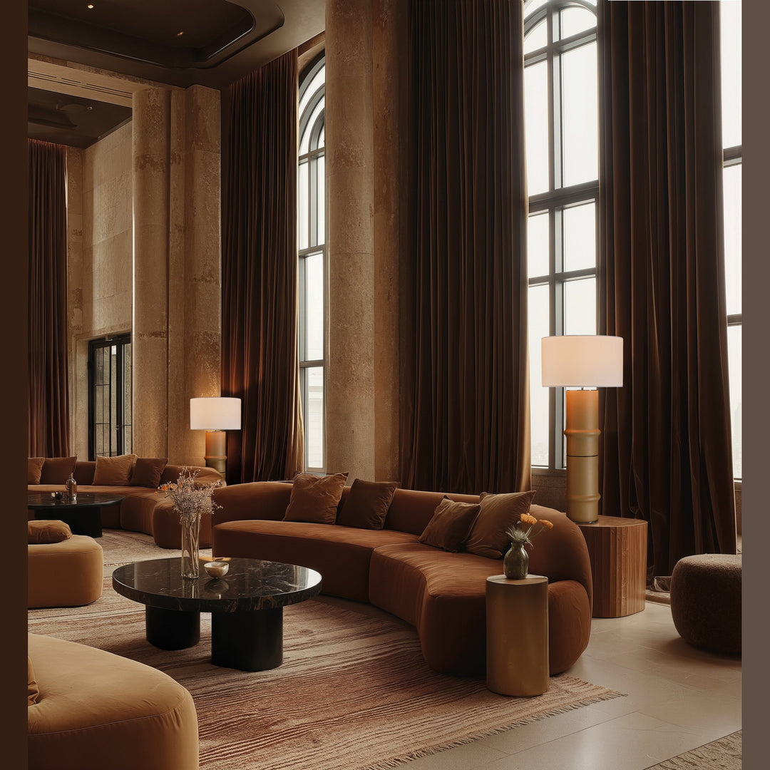 Bambu Table Lamp collection floor versions, lit, in a lofty lounge with a curved velvet sofa and brown drapes