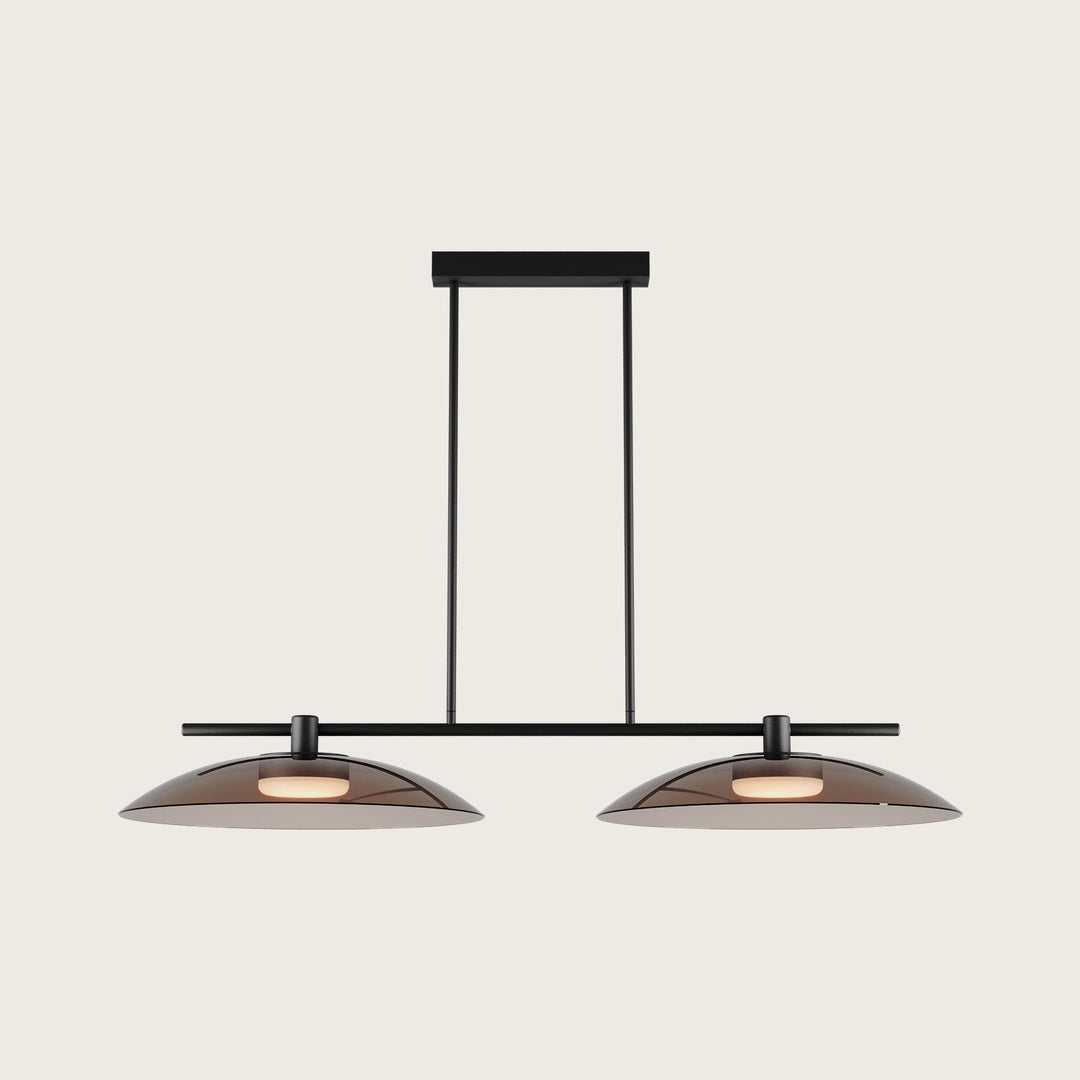 Betty Linear Pendant Linear Pendant, black bar with two wide smoked glass shades, lit, on a pale backdrop by Aromas del Campo