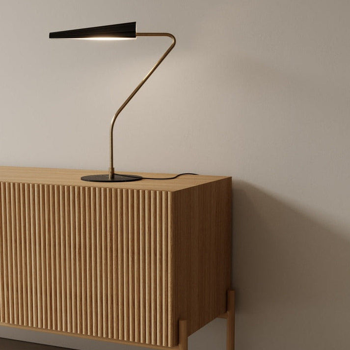 Bion Table Lamp in Matt Brass / Matt Black, lit on a fluted oak sideboard