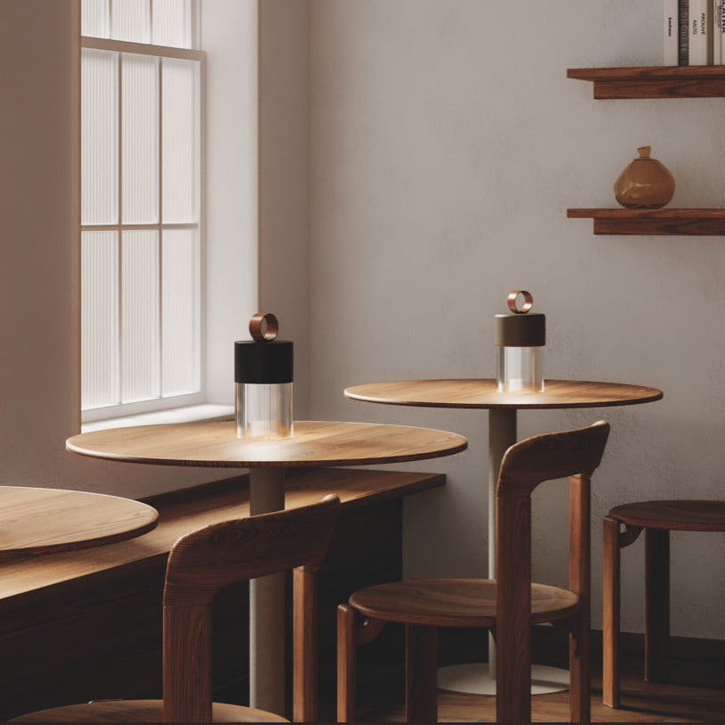 Bora C Table Lamps glowing on round wooden café tables by tall windows