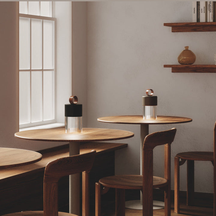 Bora M Table Lamps glowing on round wooden café tables by tall windows