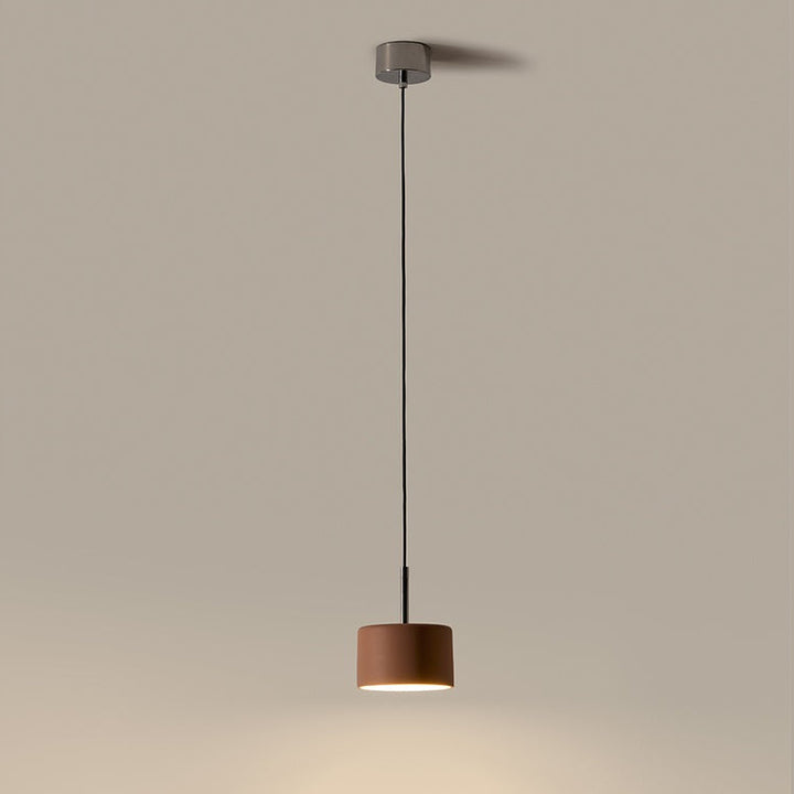 Cora Pendant Lamp lit, a rust brown ceramic drum casting a warm pool of light