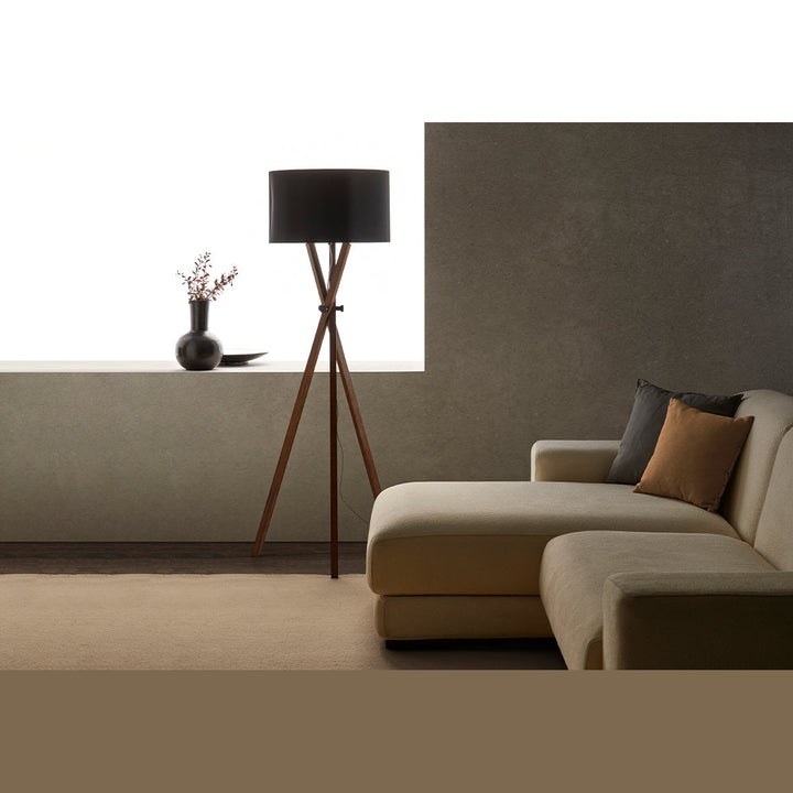 Cot Floor Lamp with black shade beside a beige sectional sofa with cushions against a dark textured wall