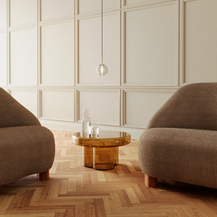 Small ribbed glass pendant hanging over a coffee table between two brown armchairs on herringbone floor