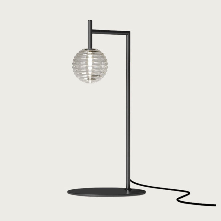 Doul Table Lamp with its clear ribbed glass sphere glowing on an angled black arm and round base