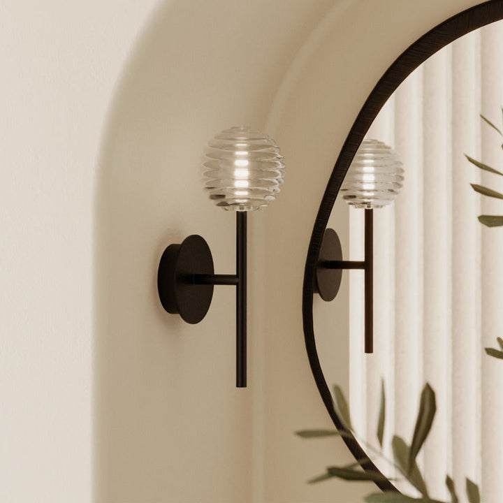 Doul Wall Lamp in black beside an arched mirror reflecting olive branches