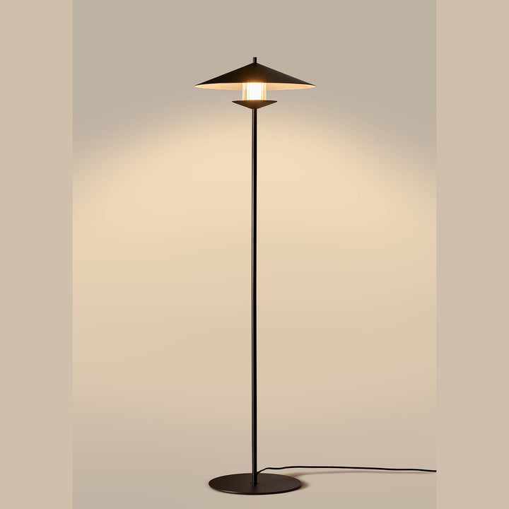 Lit black conical floor lamp casting warm light on a beige wall